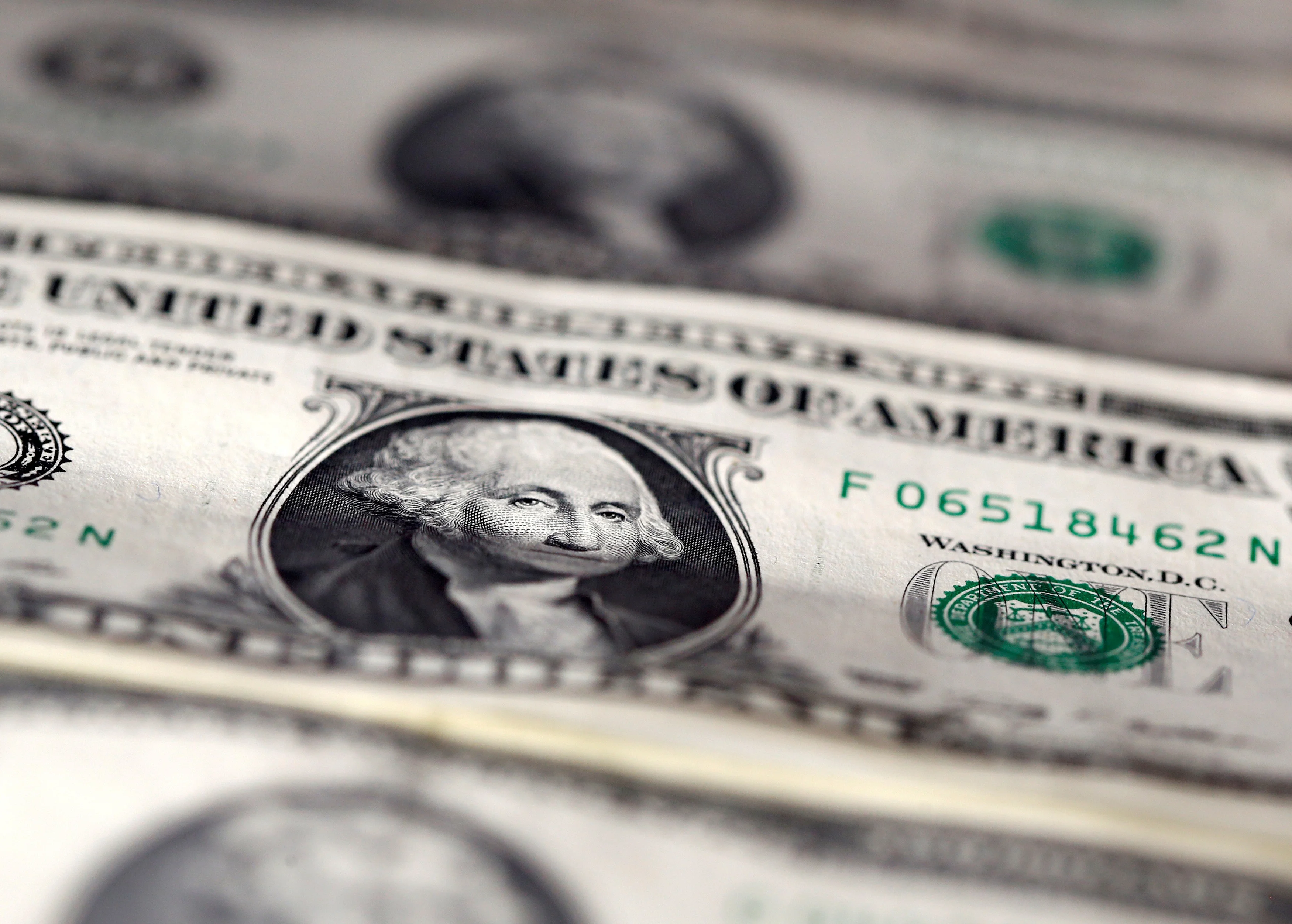 Uma mão segura uma nota de dólar americano enquanto, ao fundo, um gráfico de barras financeiro exibe tendências de queda e um mapa-múndi desfocado destaca o Oriente Médio, simbolizando a tensão geopolítica e seu impacto nos mercados.