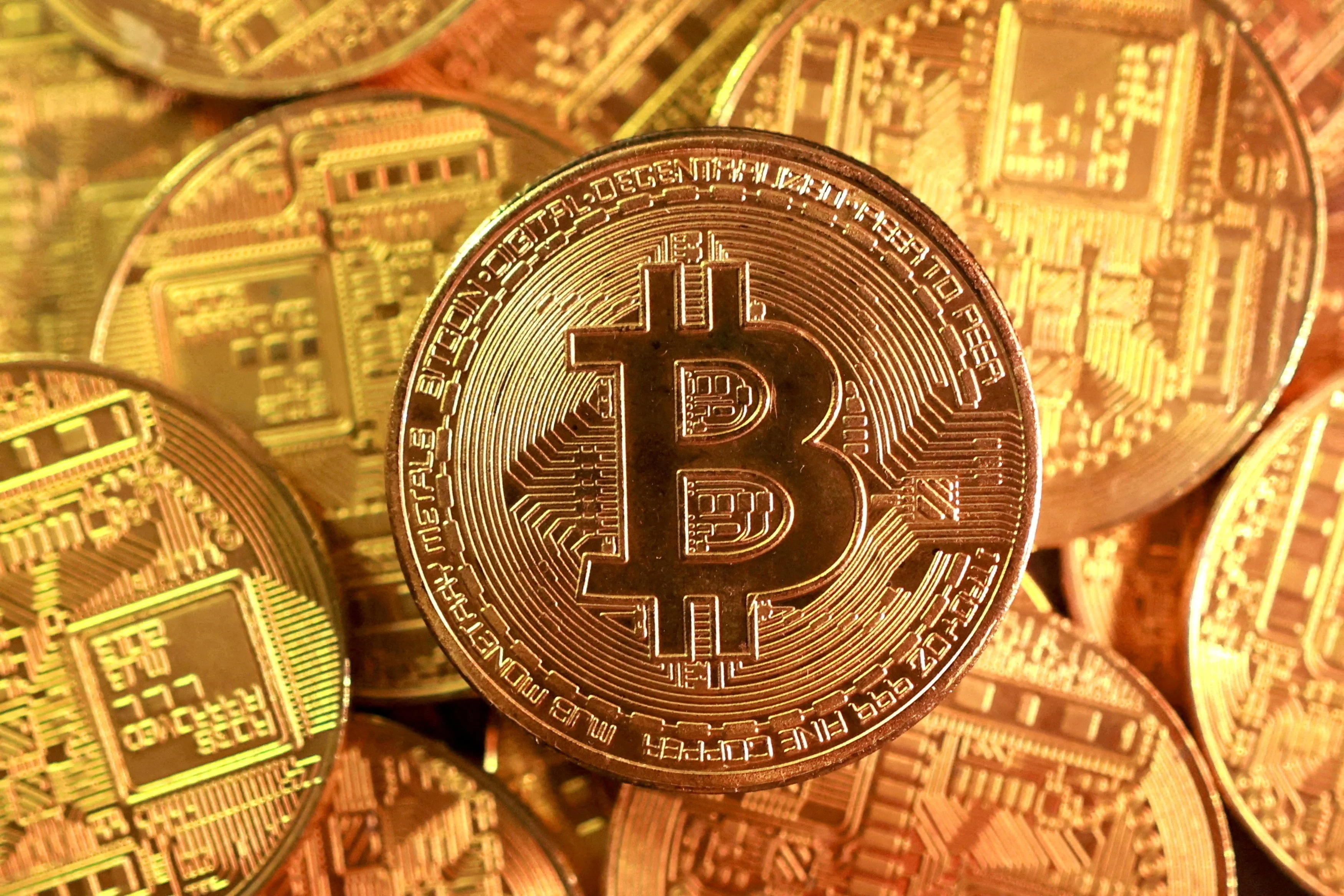 Uma ilustração digital de uma moeda Bitcoin dourada e brilhante, com o símbolo 'B' no centro, emergindo de uma grade de circuitos digitais azuis e roxos, simbolizando a natureza tecnológica e misteriosa da criptomoeda.