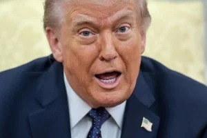 Donald Trump, um homem mais velho com cabelos loiros e terno escuro, em um pódio, gesticulando. Ao fundo, uma bandeira americana e uma alemã se entrelaçam com símbolos de conflito, como mapas e gráficos de volatilidade financeira.